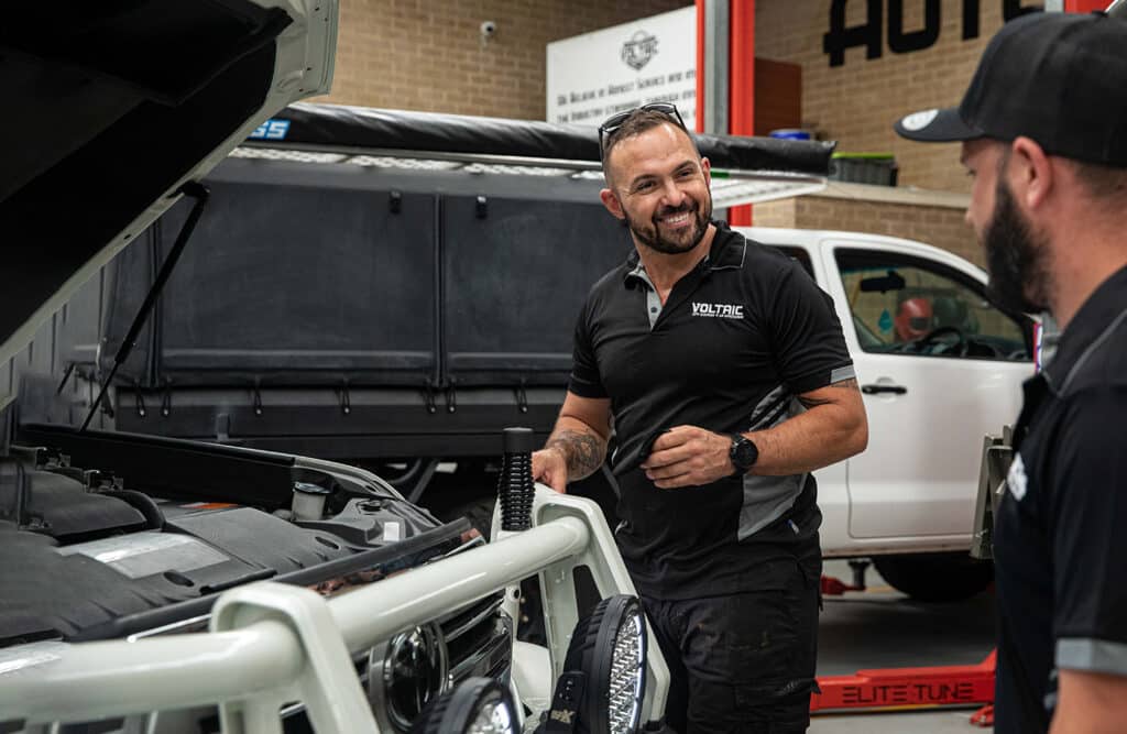 Josh, the owner of Voltaic smiling as he helps his employee perform a vehicle service in the workshop