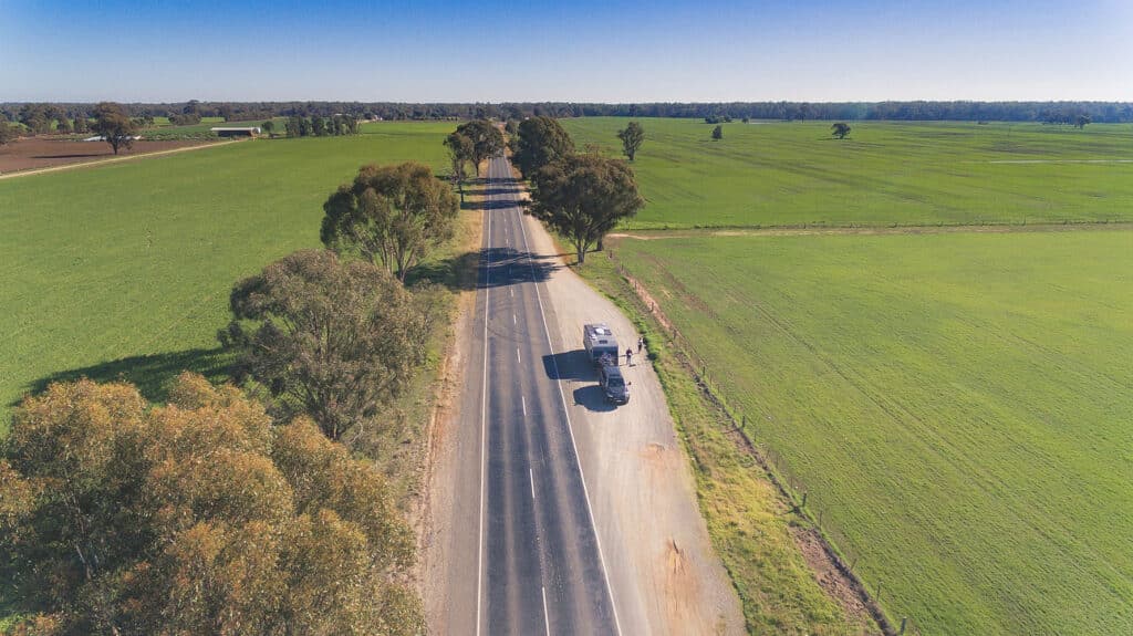 A big car pulling over with a caravan on the side of a rural Australian road.